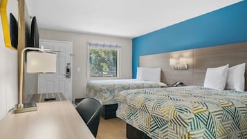 Une chambre d’hôtel avec deux lits, un bureau, une chaise, une lampe de bureau, une fenêtre donnant sur des arbres et une porte avec une pancarte.