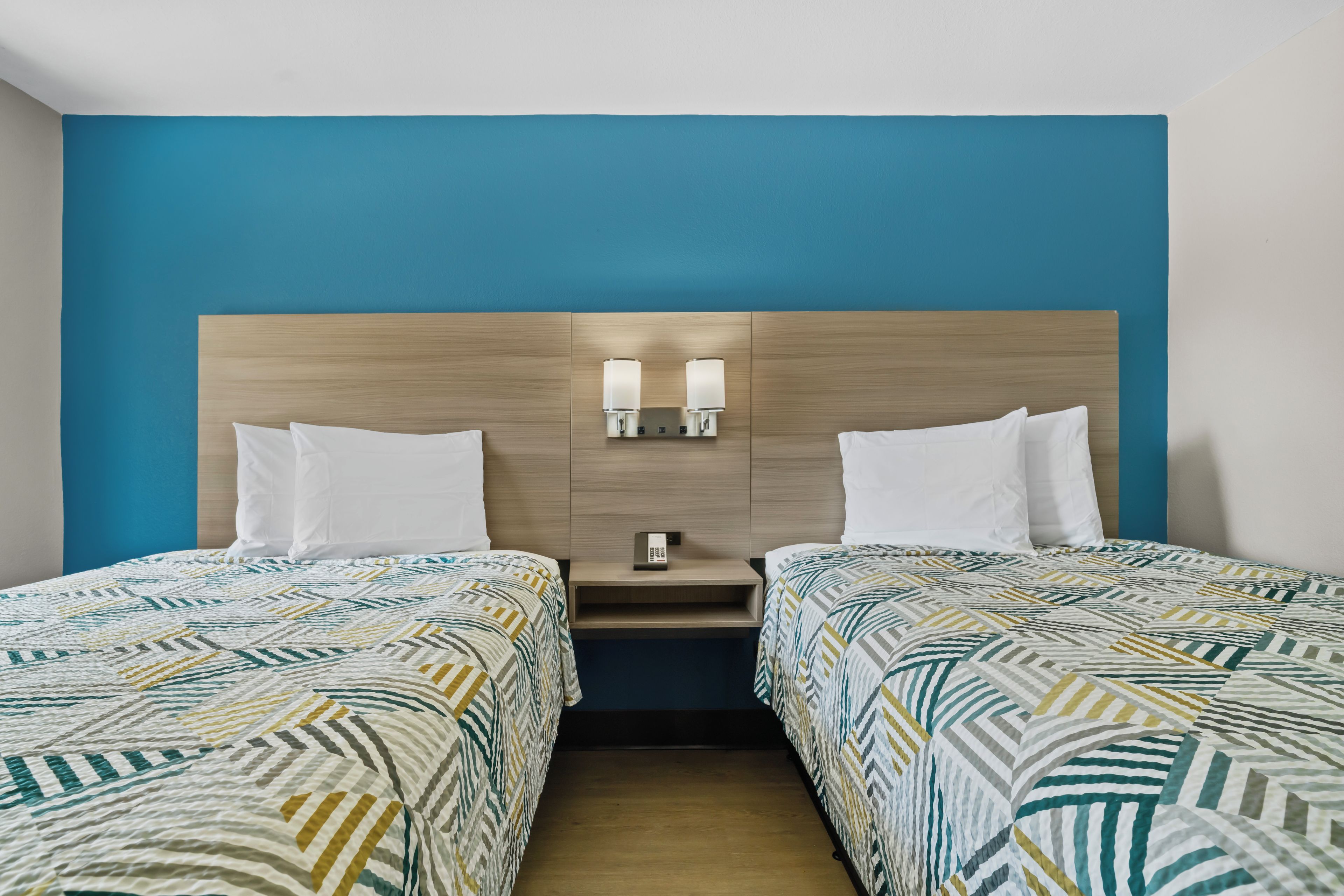 A hotel room with two beds, a wooden headboard, bedside lamps, and a phone on the nightstand.