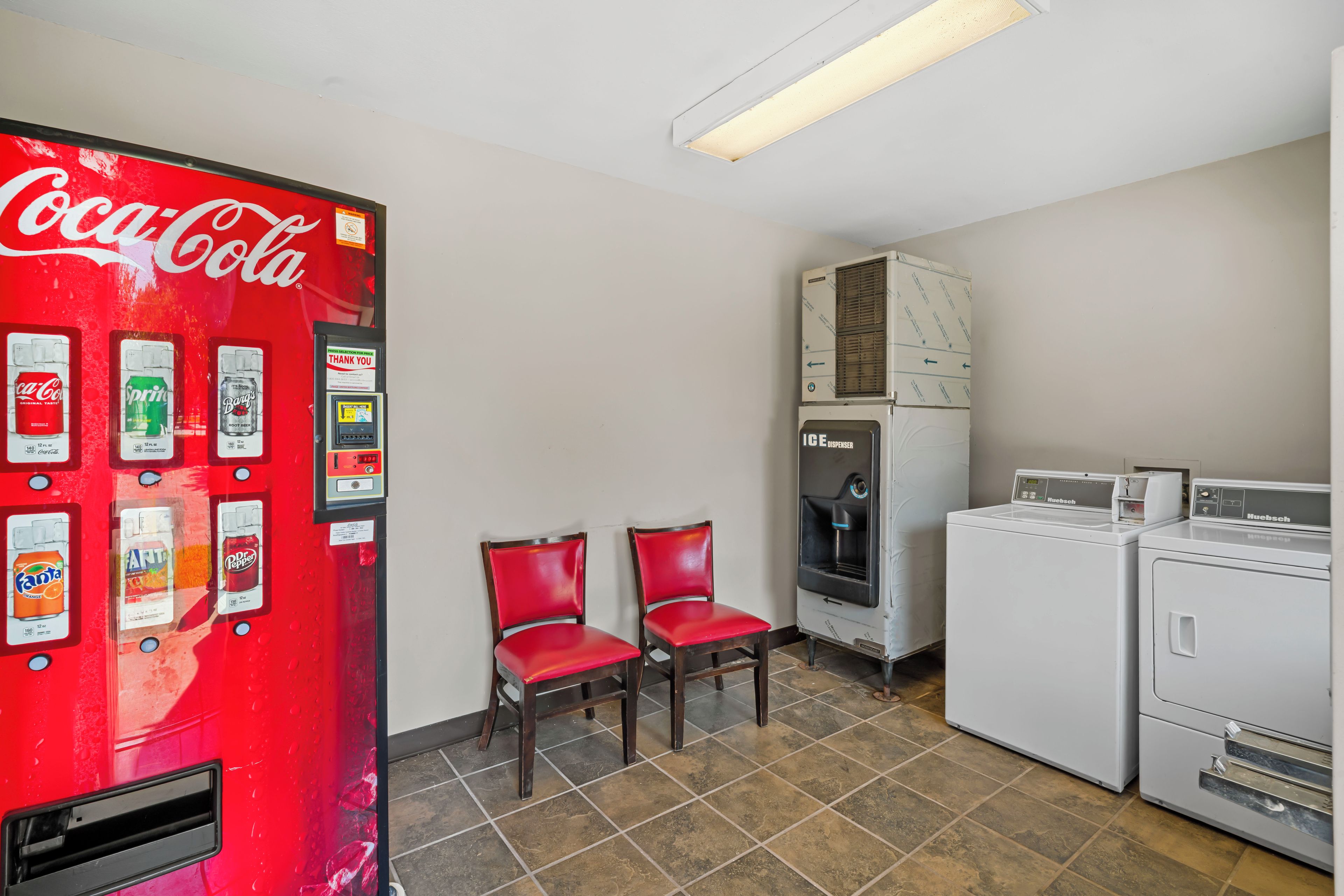 Habitación con máquina expendedora de Coca-Cola, dos sillas rojas, dispensador de agua y lavadora.