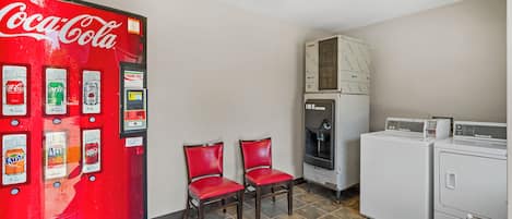 A room with a Coca-Cola vending machine, two red chairs, a water dispenser, and a washing machine.