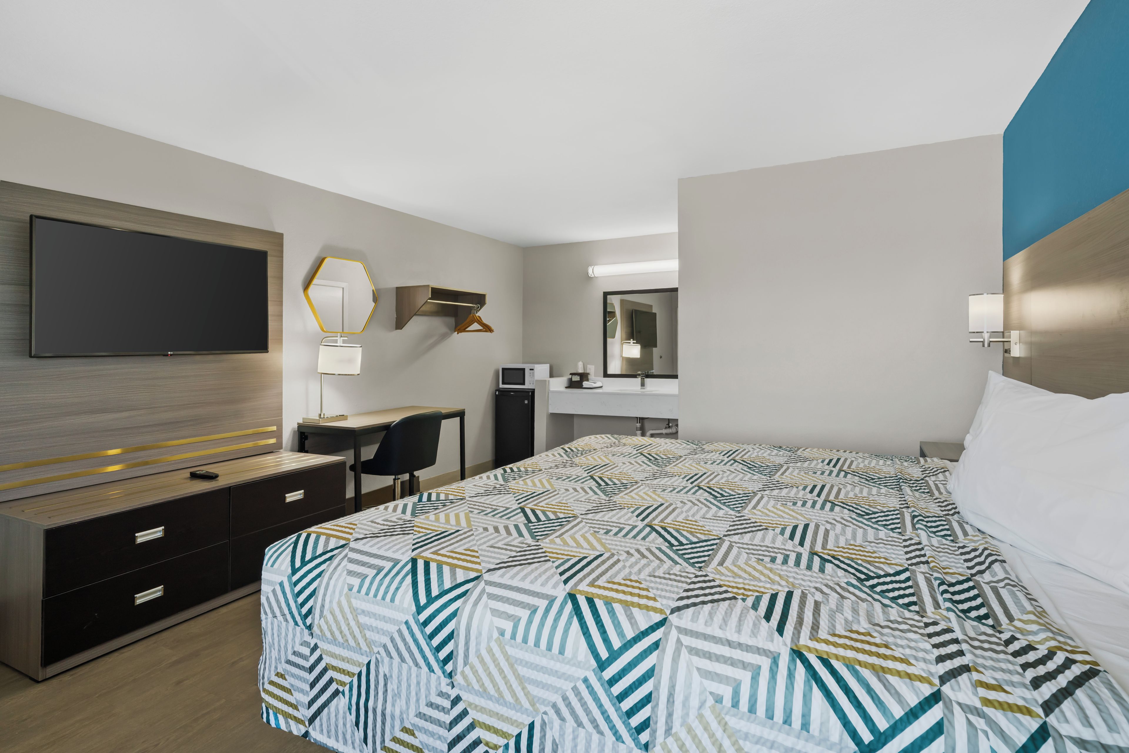 A hotel room with a bed, a desk, a TV, and a mirror.