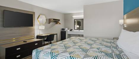 A hotel room with a bed, a desk, a TV, and a mirror.