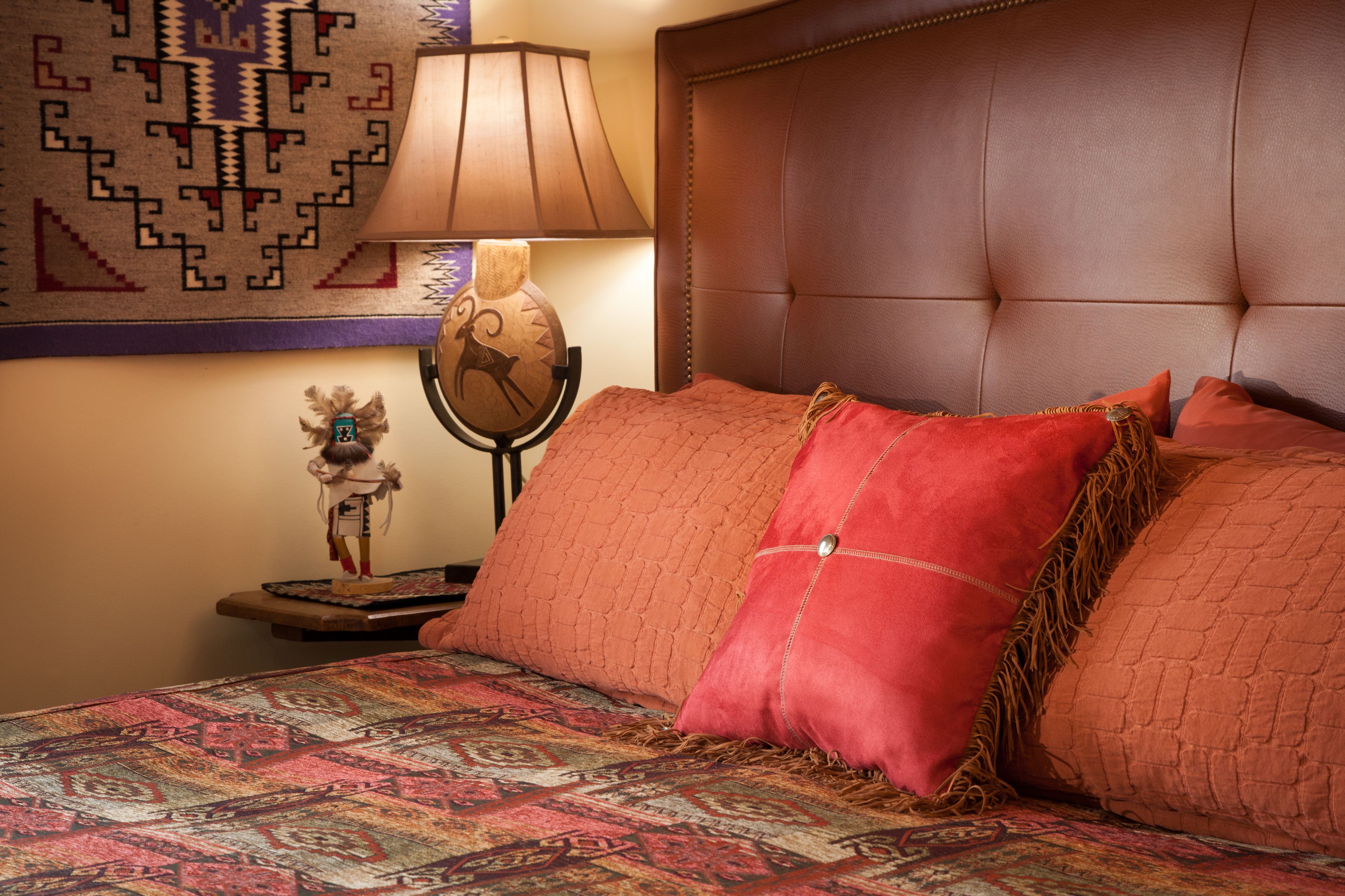 A bed with a patterned bedspread, a headboard, and a nightstand with a lamp and a decorative item.