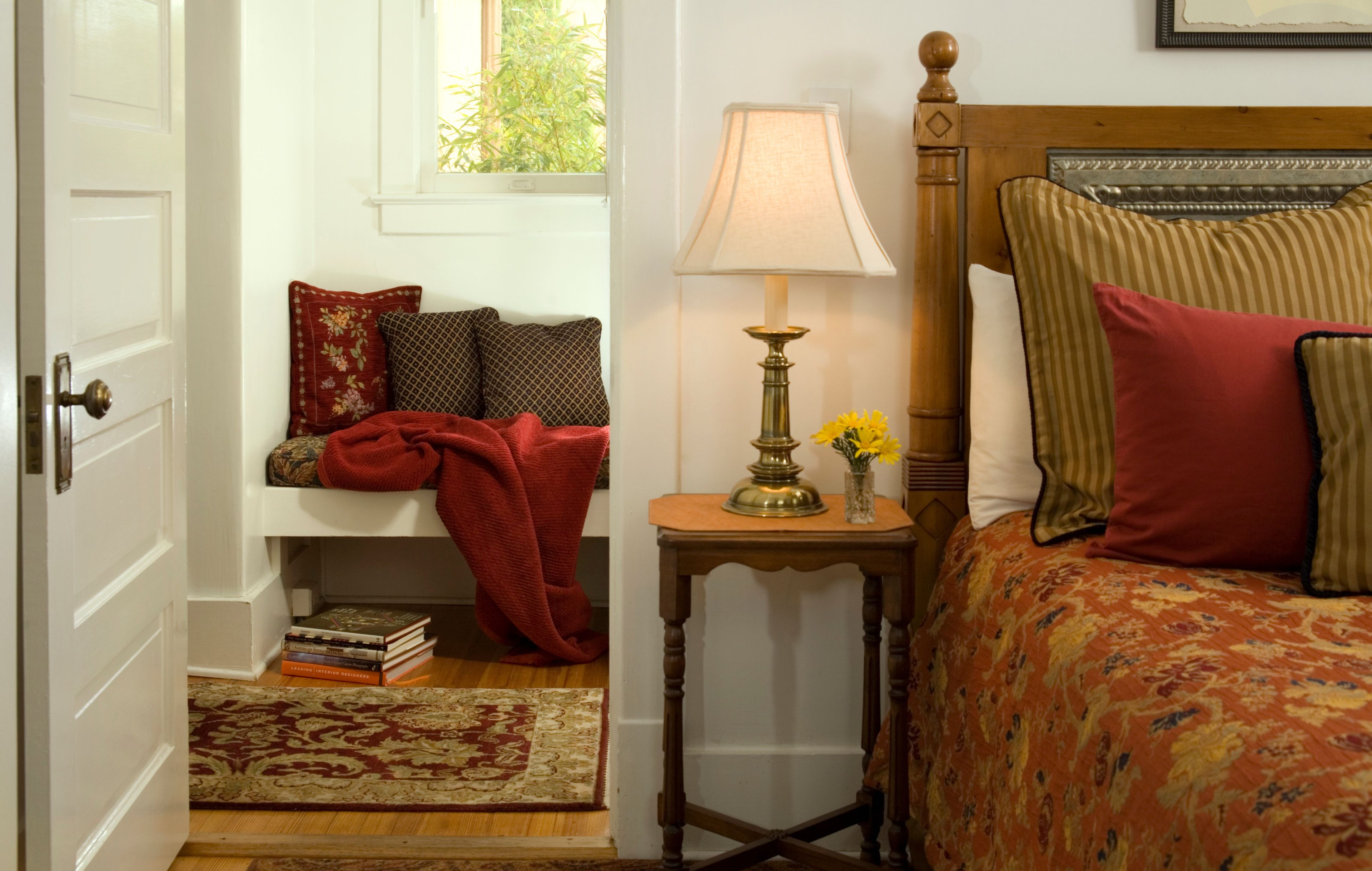 A bedroom with a bed, a nightstand, a lamp, a window, and a door.