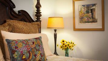 Una cama bien hecha con almohadas estampadas, una lámpara de noche y un florero con girasoles.