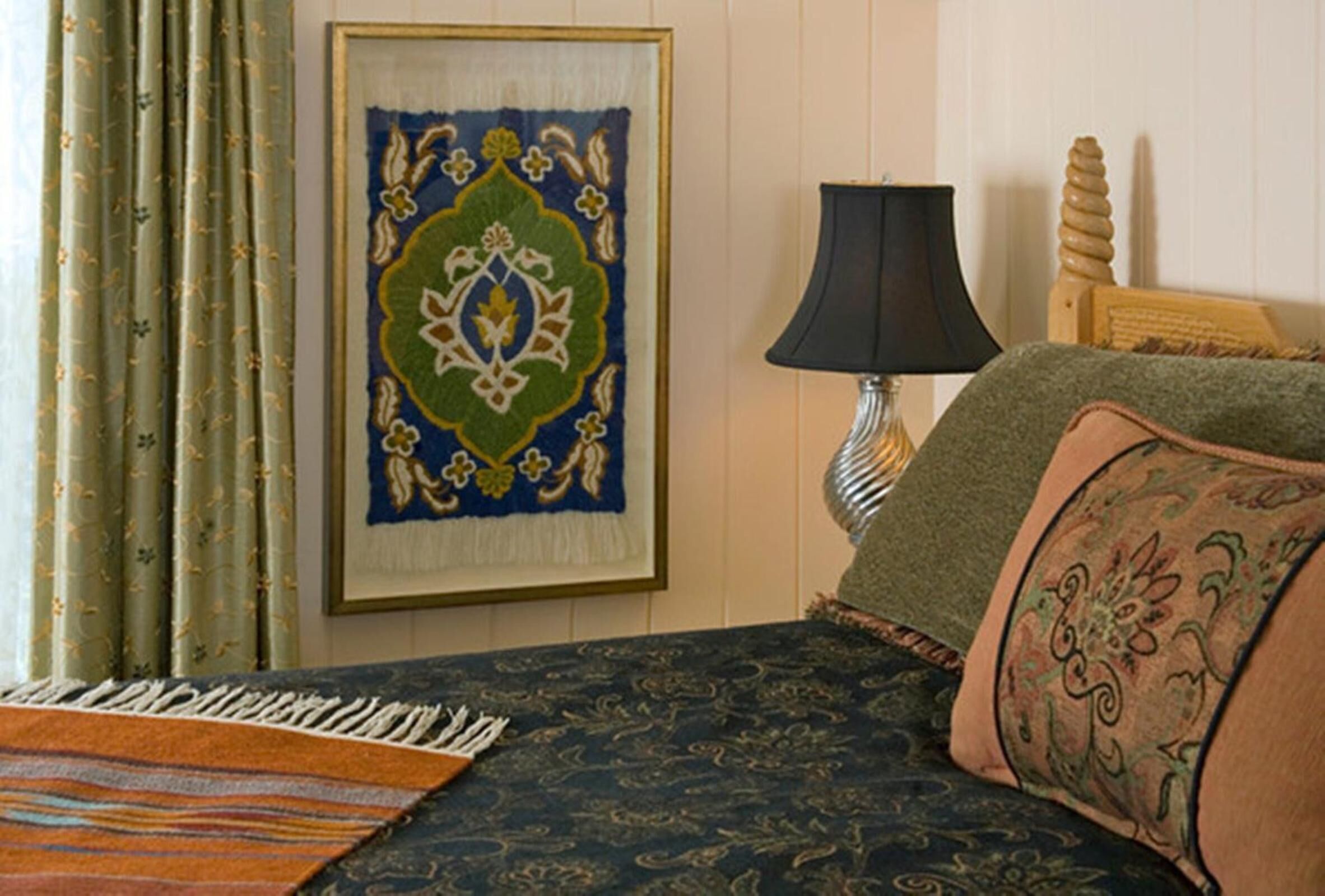Una habitación con una cama, un tapiz enmarcado, una lámpara y un cabecero de madera.