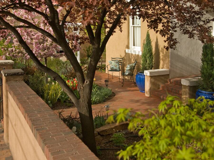 A garden with a brick wall, a tree with pink blossoms, and a blue planter.