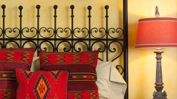 A bed with a metal headboard, multiple pillows, a decorative wall hanging, and a bedside lamp.