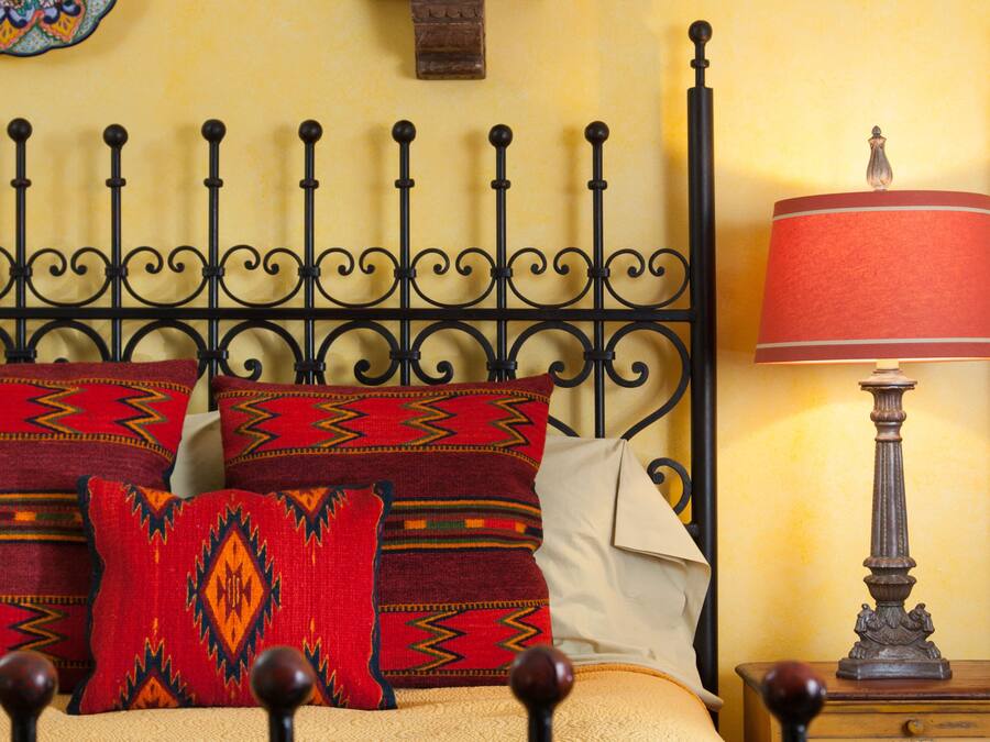 A bed with a metal headboard, multiple pillows, a decorative wall hanging, and a bedside lamp.