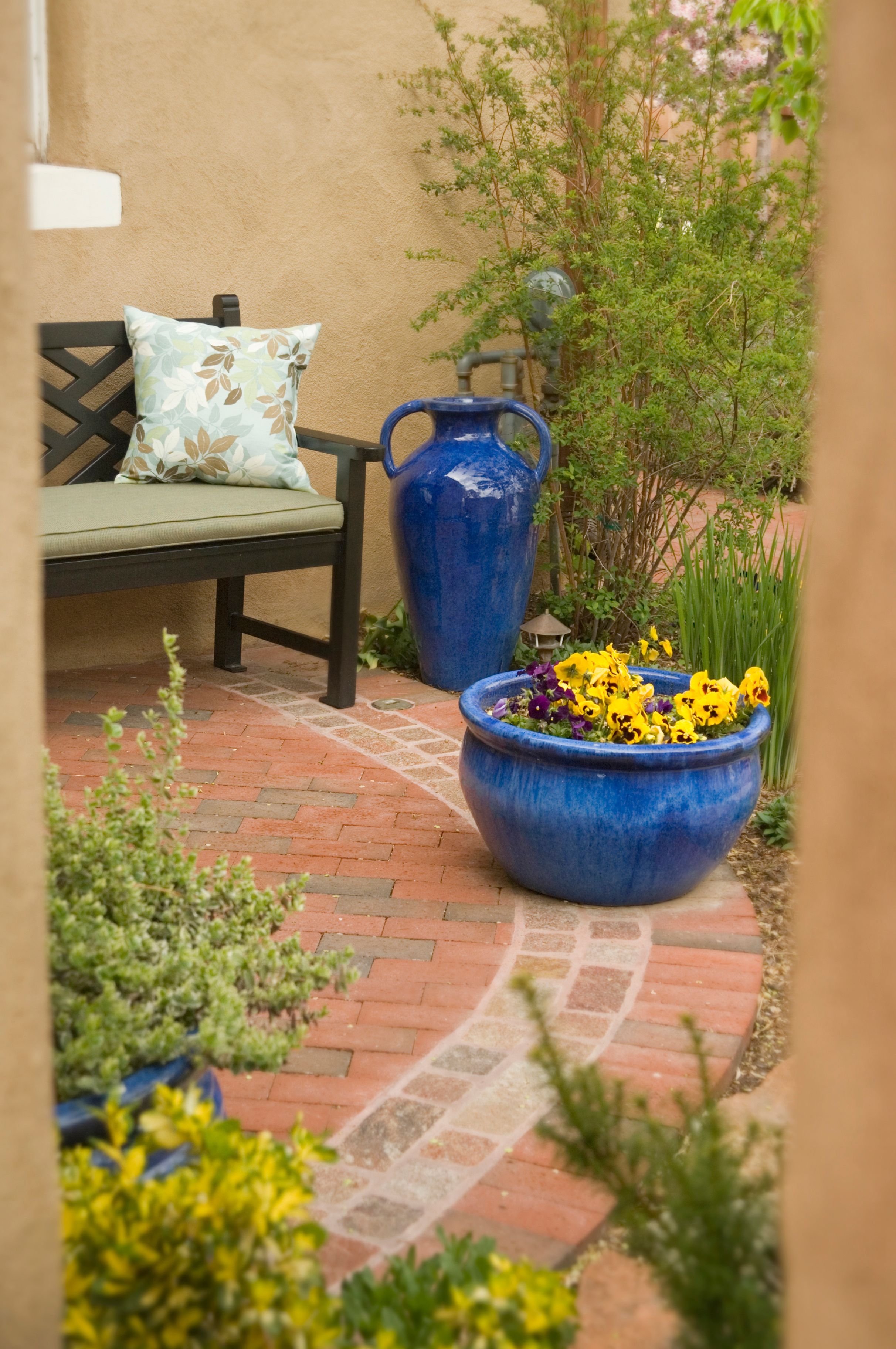 Un patio con un banco, una maceta azul grande con flores y un camino de ladrillo.