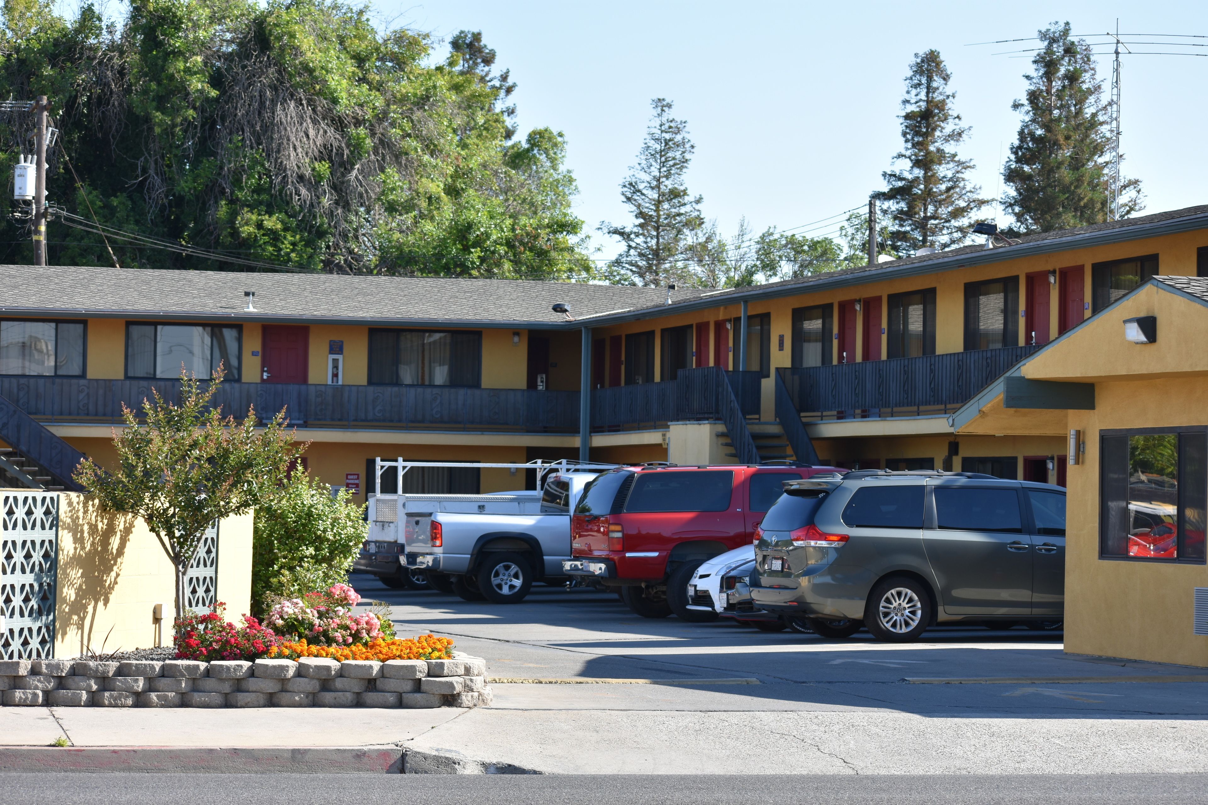 Un motel avec une rangée de chambres, un parking et un petit jardin agrémenté de fleurs.