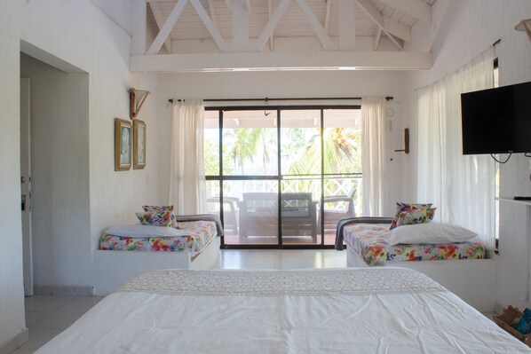 A hotel room with two single beds, a large bed, a TV, and a sliding glass door to a balcony. - Ocean View Sai (San Andrés)