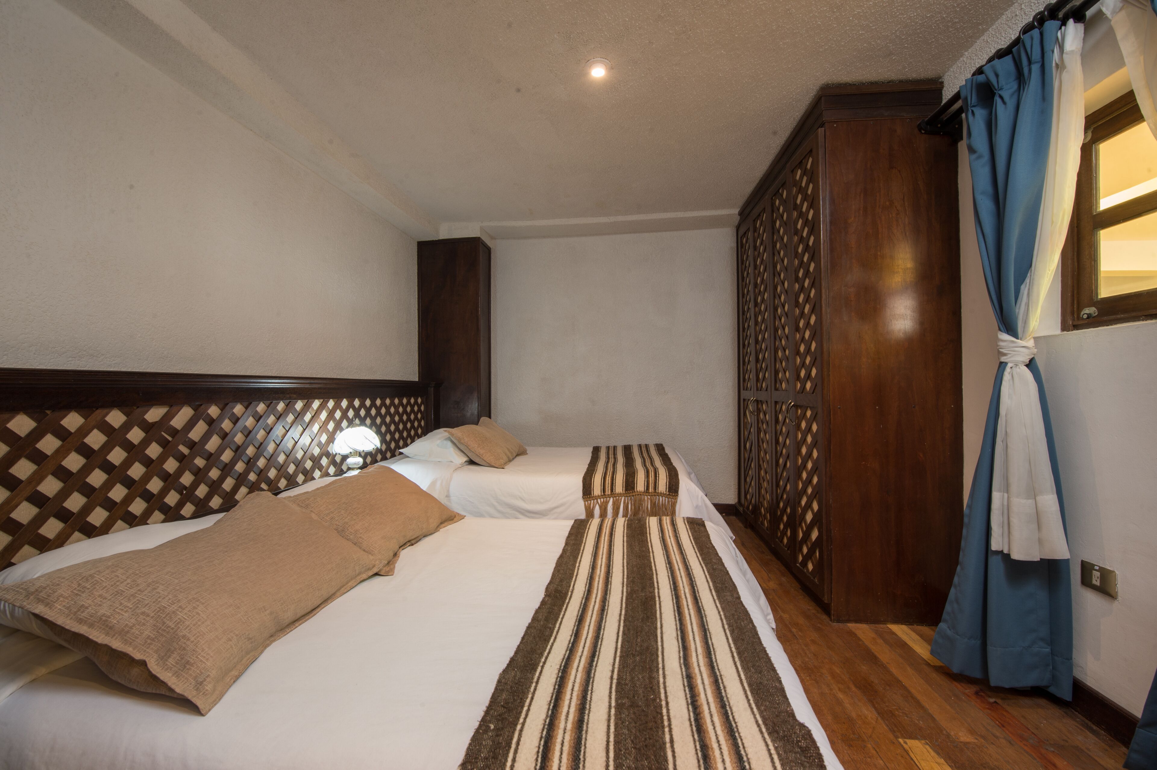Habitación de hotel con dos camas, cabeceros de madera, un armario y una ventana con cortinas.