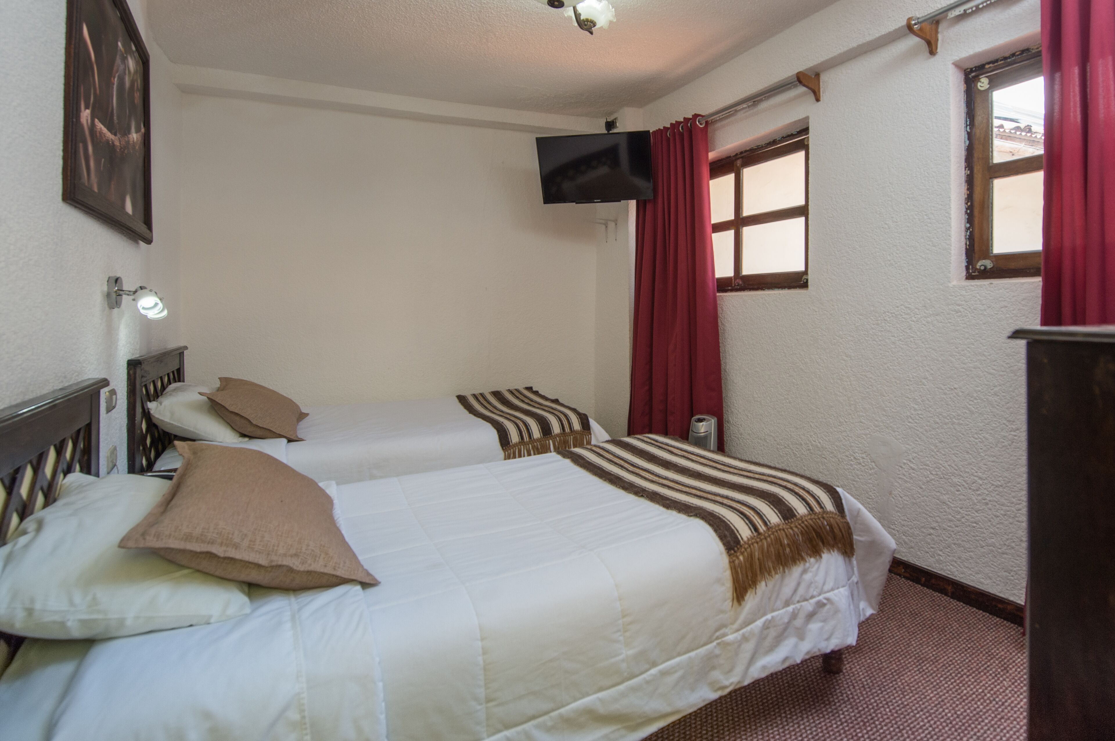 Ein Hotelzimmer mit zwei Betten, einem an der Wand montierten Fernseher und einem Fenster mit Vorhängen.