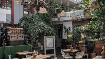 A spacious indoor area with tables and chairs, a chandelier, and hanging plants.