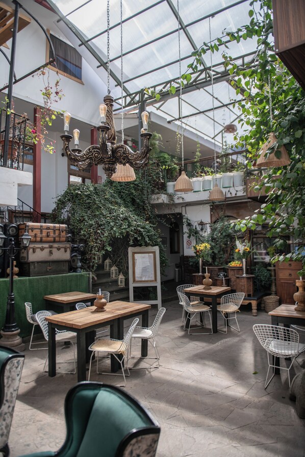 Un espacio interior amplio con mesas y sillas, un candelabro y plantas colgantes.