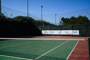 Una cancha de tenis con una red, rodeada por una cerca verde y carteles publicitarios.