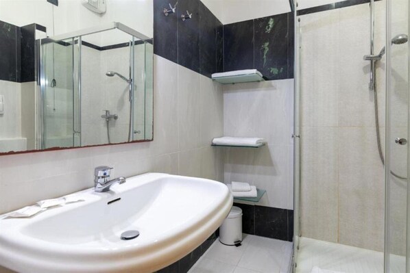 Un baño con un lavamanos blanco, una cabina de ducha de vidrio y un espejo.