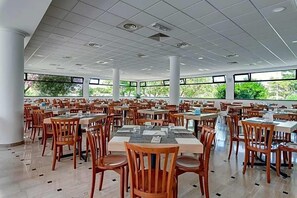 Un comedor amplio con varias mesas y sillas, ventanas grandes y un techo de baldosas.