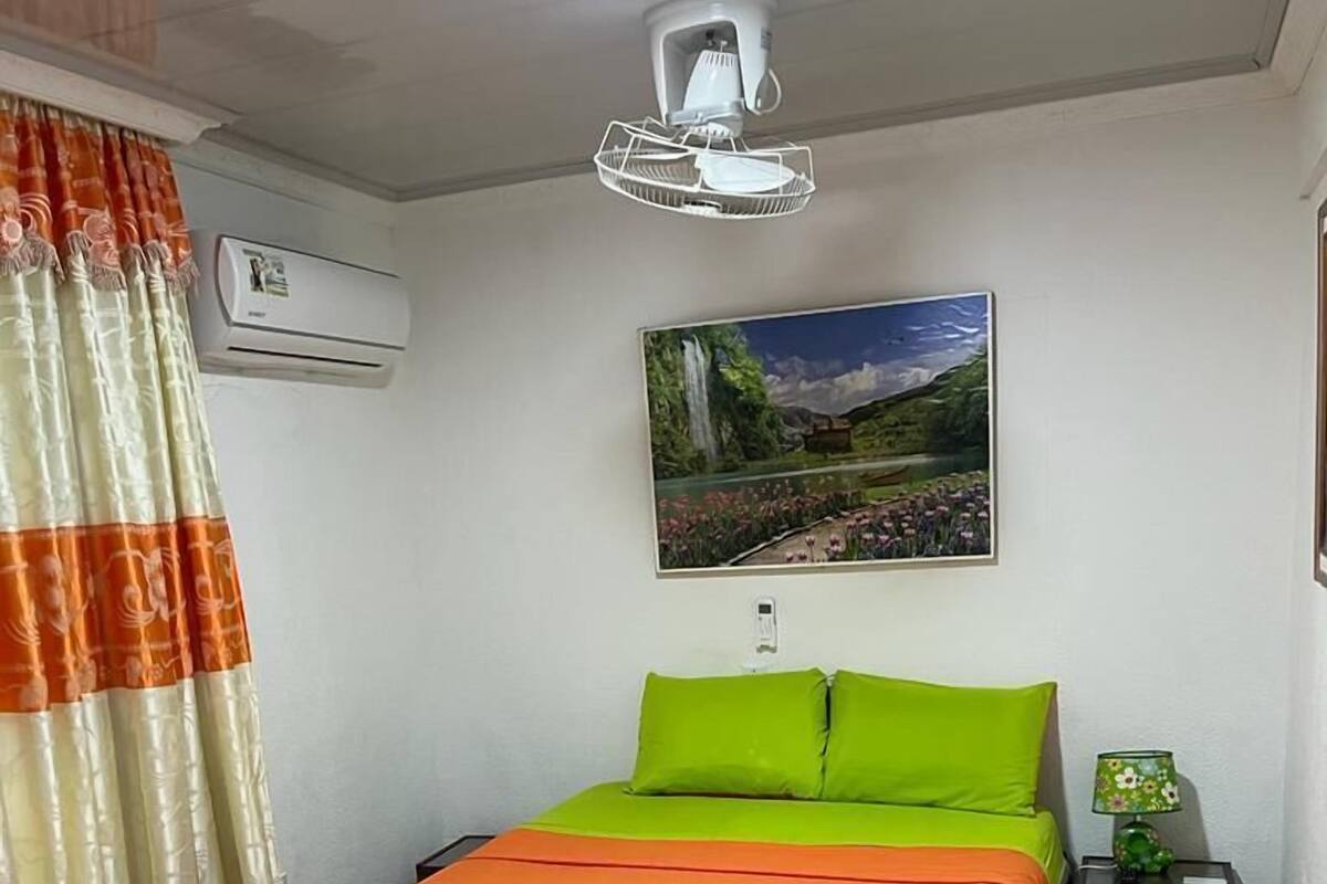 Une chambre d’hôtel avec un lit, une table de chevet, une lampe, un tableau au mur et une fenêtre avec des rideaux.