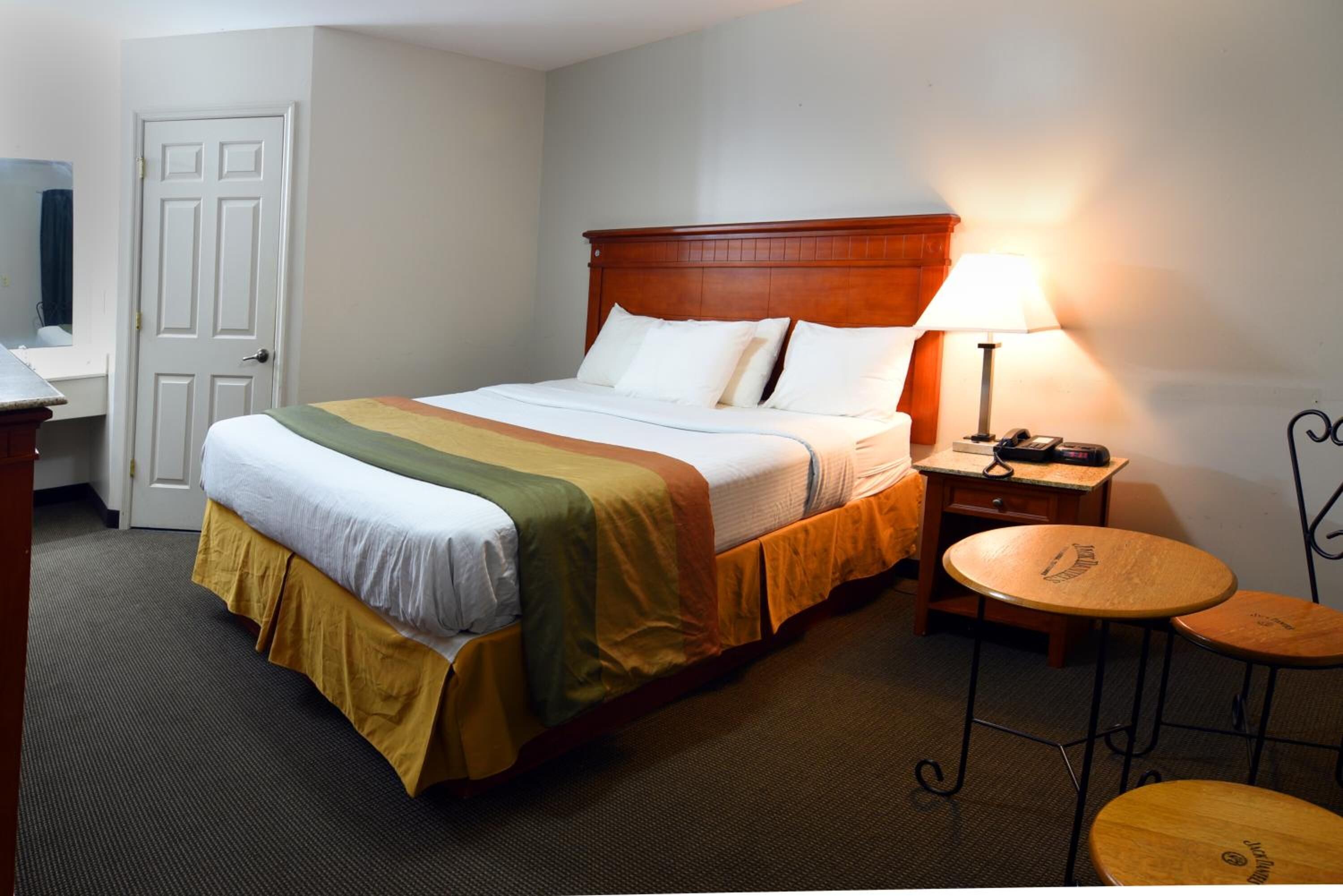 A hotel room with a bed, a nightstand, a lamp, and two small round tables.