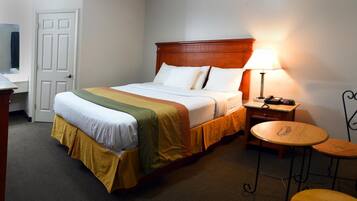 Una habitación de hotel con una cama, una mesita de noche, una lámpara y dos mesitas redondas.