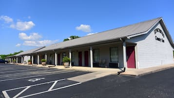 A motel with a row of rooms, a covered parking area, and a clear blue sky.