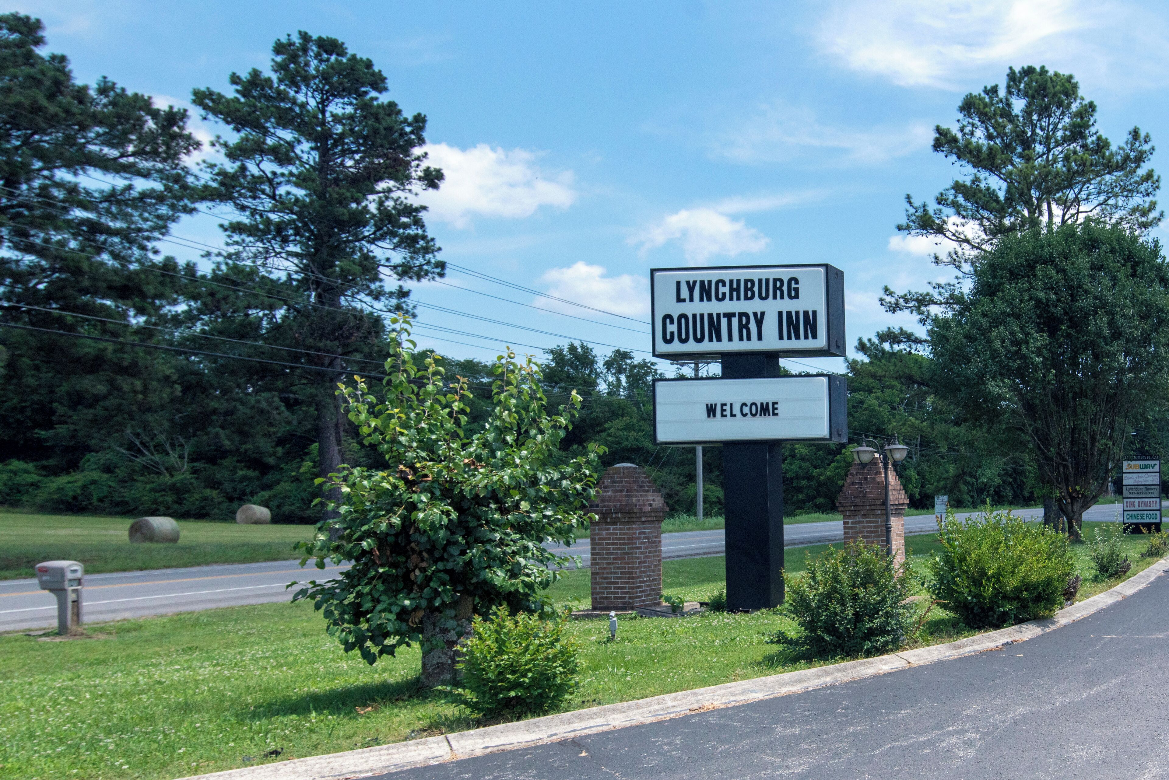 Señal de bienvenida del Lynchburg Country Inn, con una carretera despejada y follaje en el fondo.