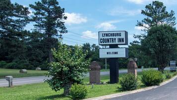 Señal de bienvenida del Lynchburg Country Inn, con una carretera despejada y follaje en el fondo.