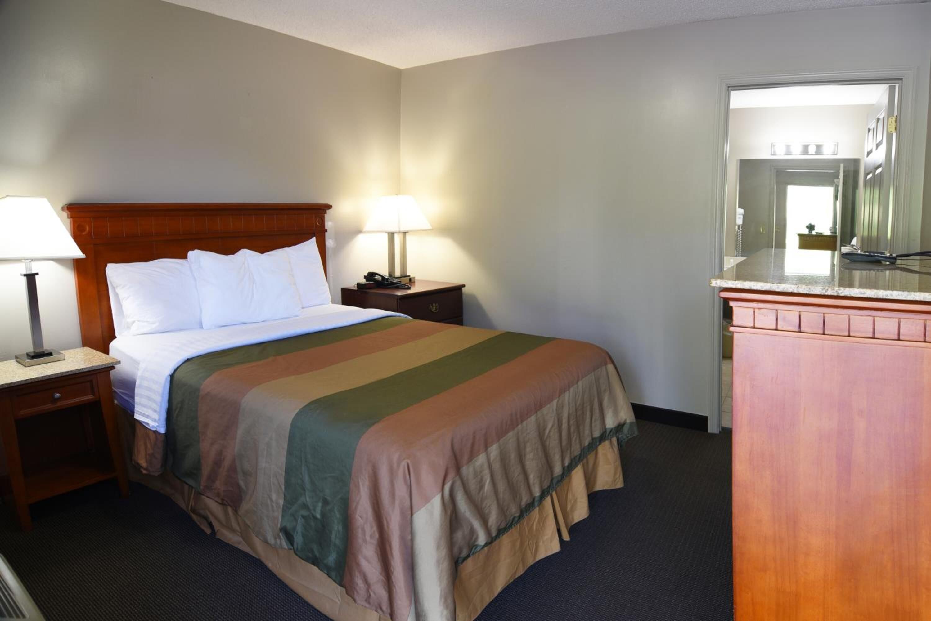 Una habitación de hotel con una cama, dos mesitas de noche con lámparas, un aparador y un espejo.