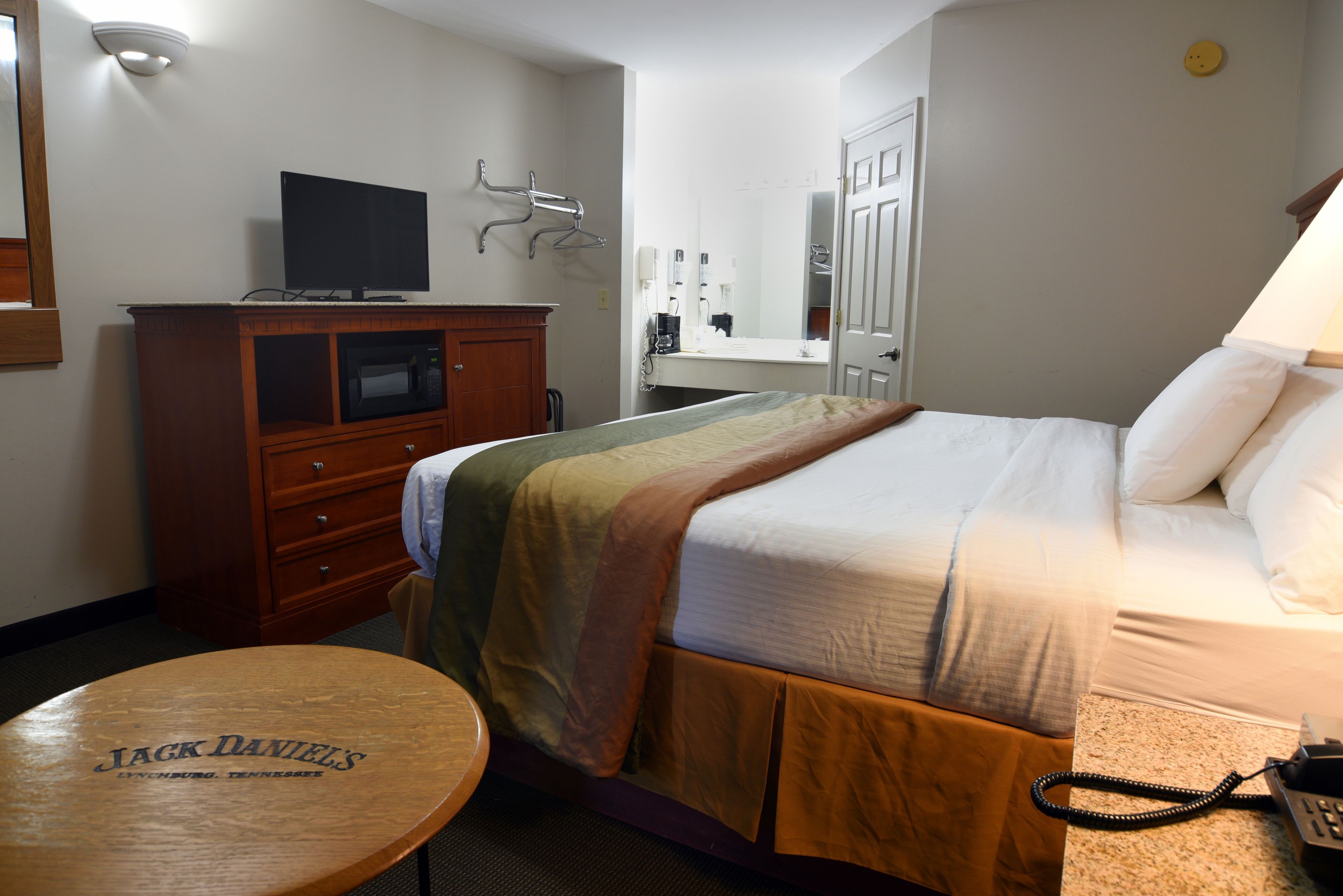 Une chambre d’hôtel avec un lit, un téléviseur posé sur un meuble en bois, une machine à café, un miroir et une table sur laquelle est posé un panneau.