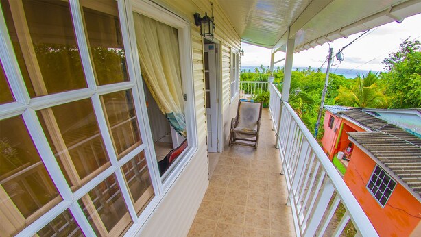 A covered balcony with a view of a lush green landscape, a wooden chair, and a small table. - Posada Nativa Atardecer Isleno (San Andrés)