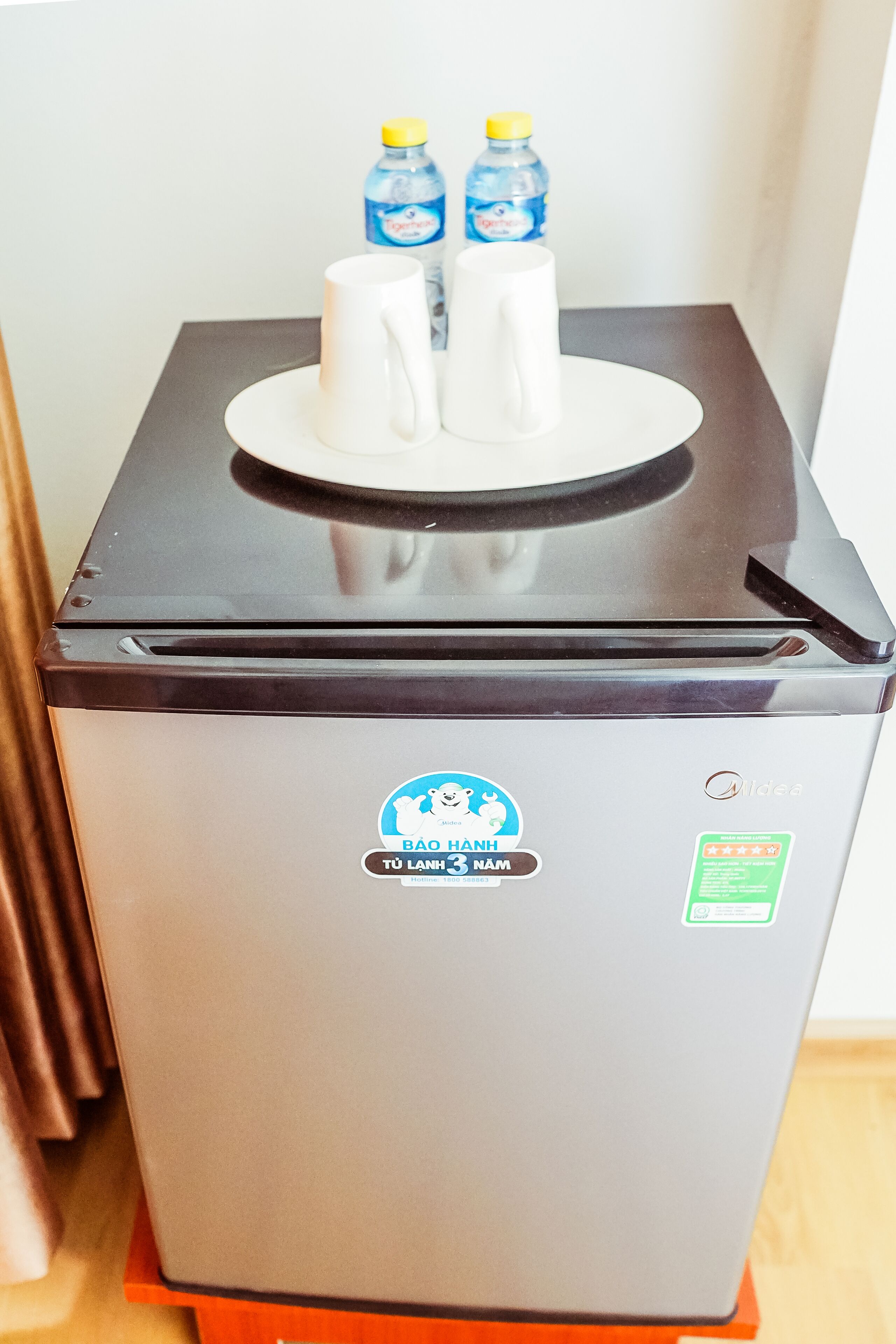 Un refrigerador compacto con dispensador de agua en la parte superior, que incluye dos botellas de agua y dos tazas blancas.