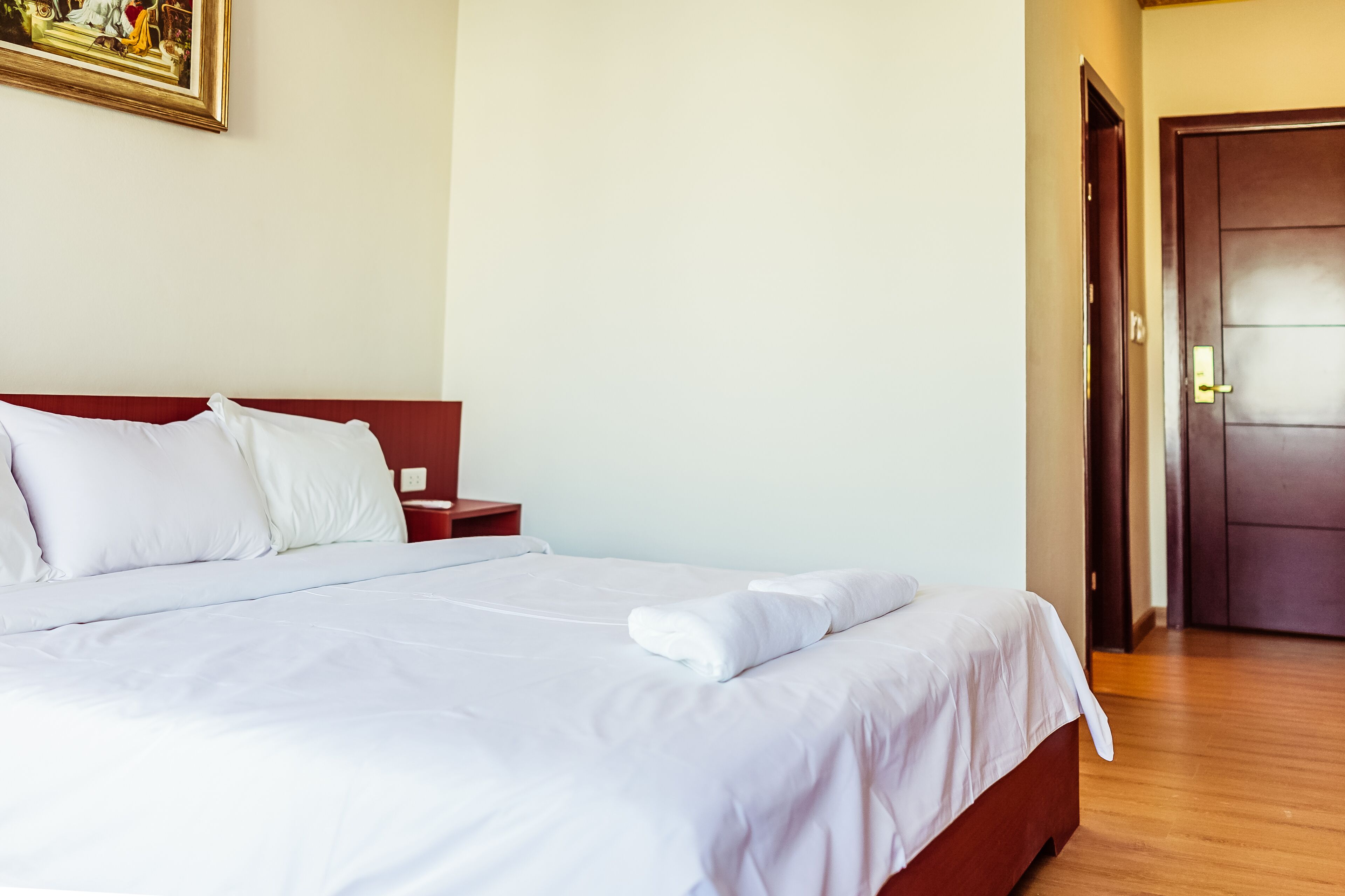A neatly made bed with white linens, a wooden headboard, and a nightstand with a lamp.