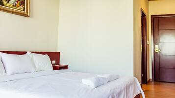 A neatly made bed with white linens, a wooden headboard, and a nightstand with a lamp.
