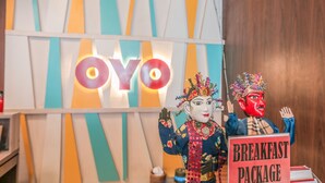 A restaurant interior with a colorful striped wall, a neon 'OYO' sign, and a 'BREAKFAST PACKAGE' sign. - Hotel Feodora Grogol (Jakarta)