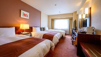A hotel room with two beds, a desk, a television, and a window with curtains.