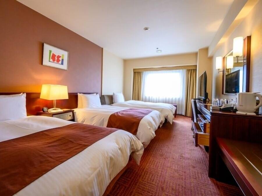 A hotel room with two beds, a desk, a television, and a window with curtains.