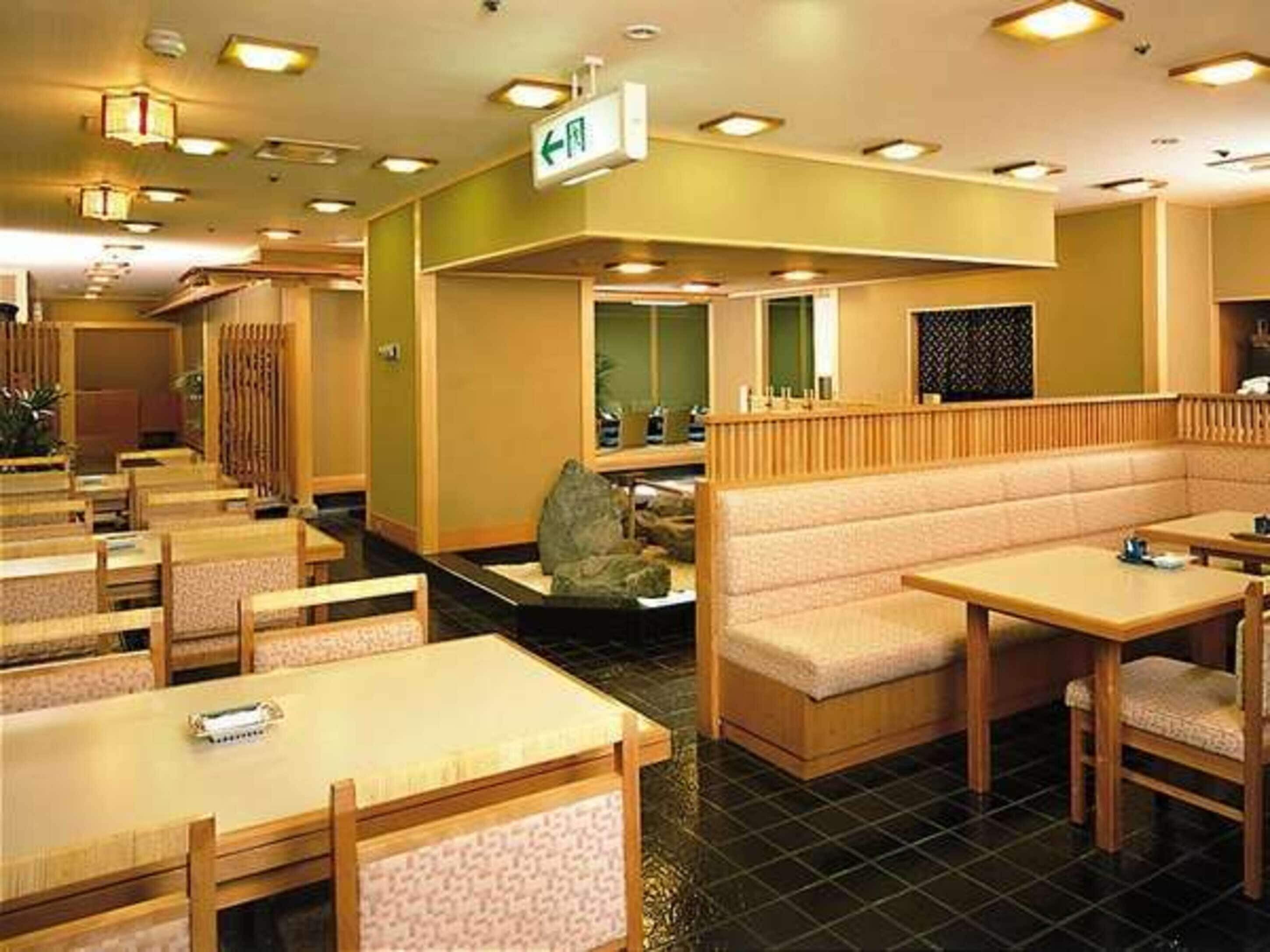 A restaurant with wooden tables and benches, a green wall with a sign, and a tiled floor.