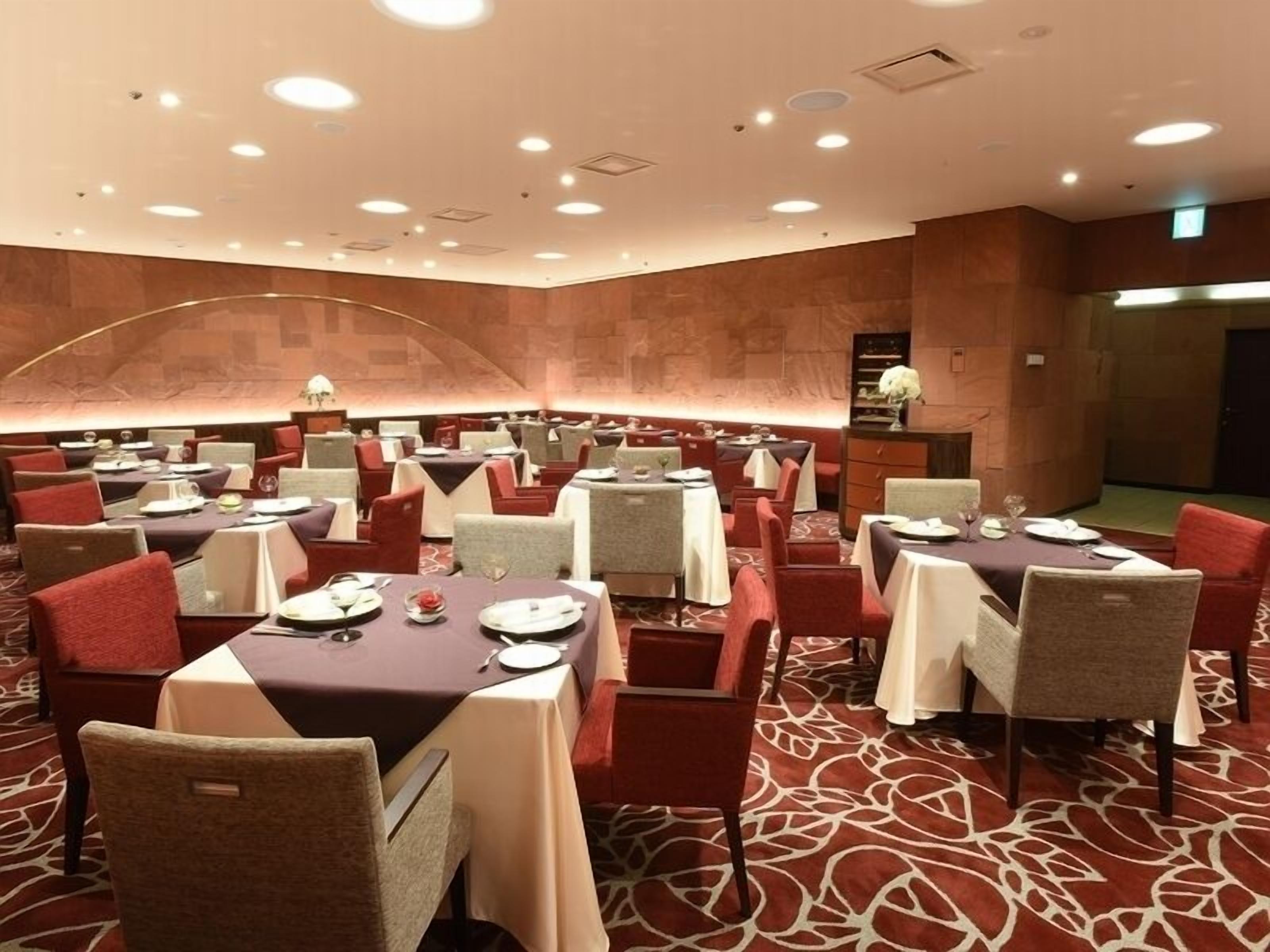 A hotel dining area with multiple tables and chairs, a patterned carpet, and a curved wall.