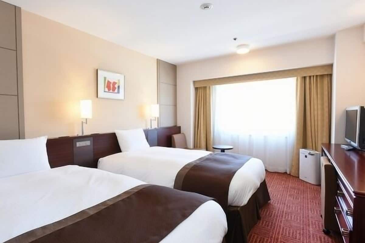 A hotel room with two beds, a desk, a television, and a window with curtains.