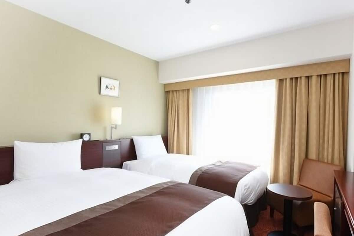 A hotel room with two beds, a desk, a chair, a lamp, and a window with curtains.