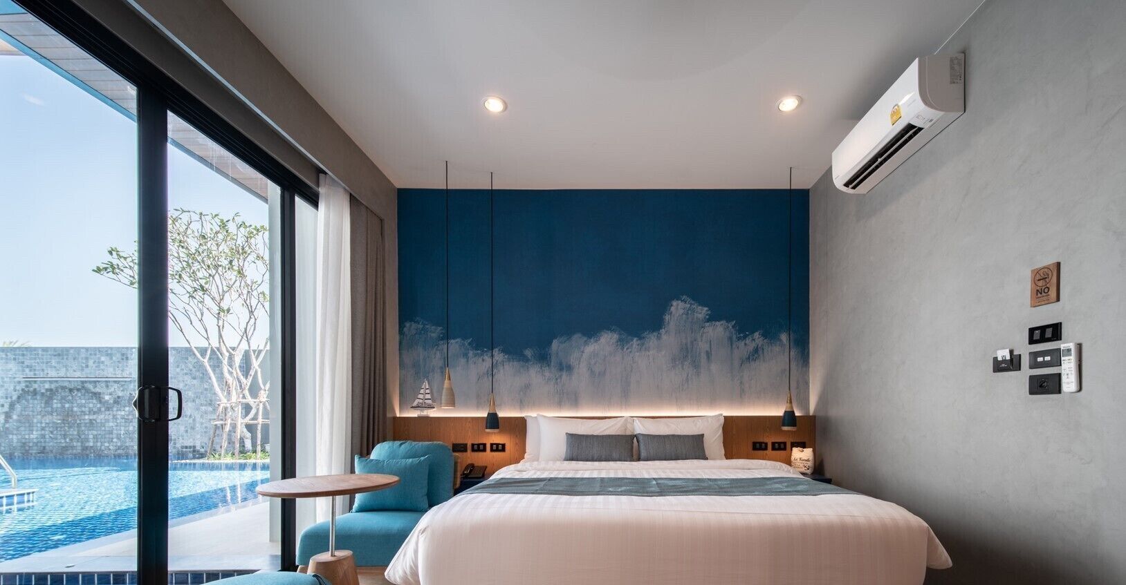 A modern hotel room with a large bed, a view of an infinity pool, and a blue accent wall.