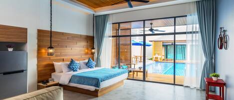 Una habitación de hotel moderna con techo de madera, una cama grande con ropa de cama azul, un sofá, una mesita y vista a una piscina al aire libre.