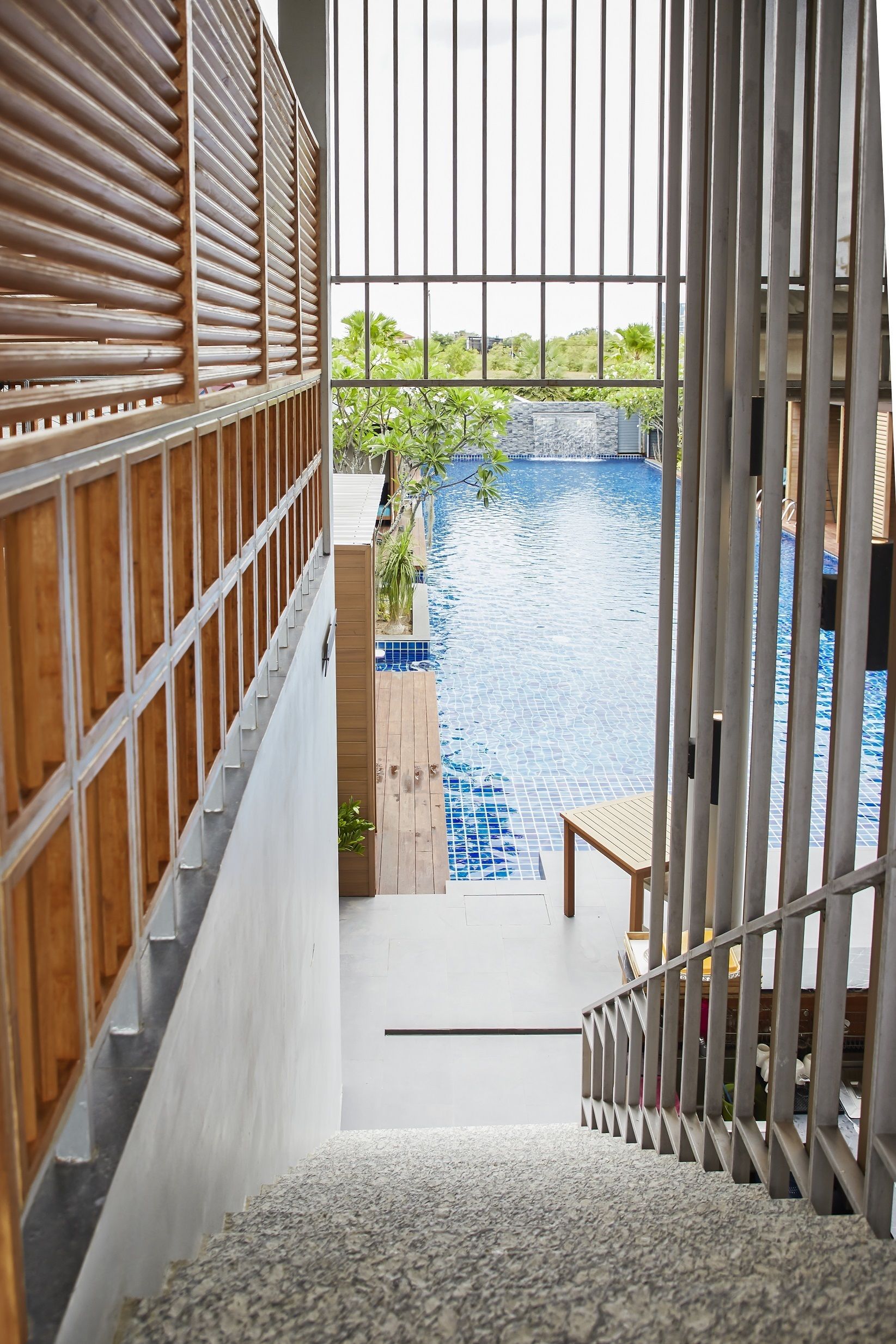 A view of a swimming pool from a staircase with a railing, surrounded by wooden paneling and a tiled floor.