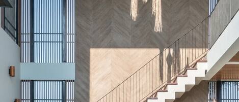 A modern interior with a staircase leading to a balcony, large windows, and hanging light fixtures.