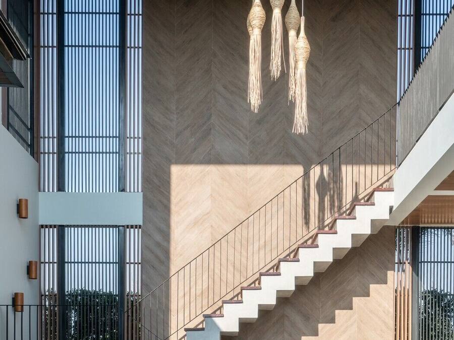 Un interior moderno con una escalera que conduce a un balcón, ventanas amplias y lámparas colgantes.