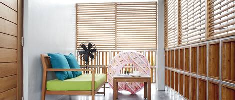 A small, cozy room with a wooden bed, a green cushion, a small table, and a decorative wall panel.