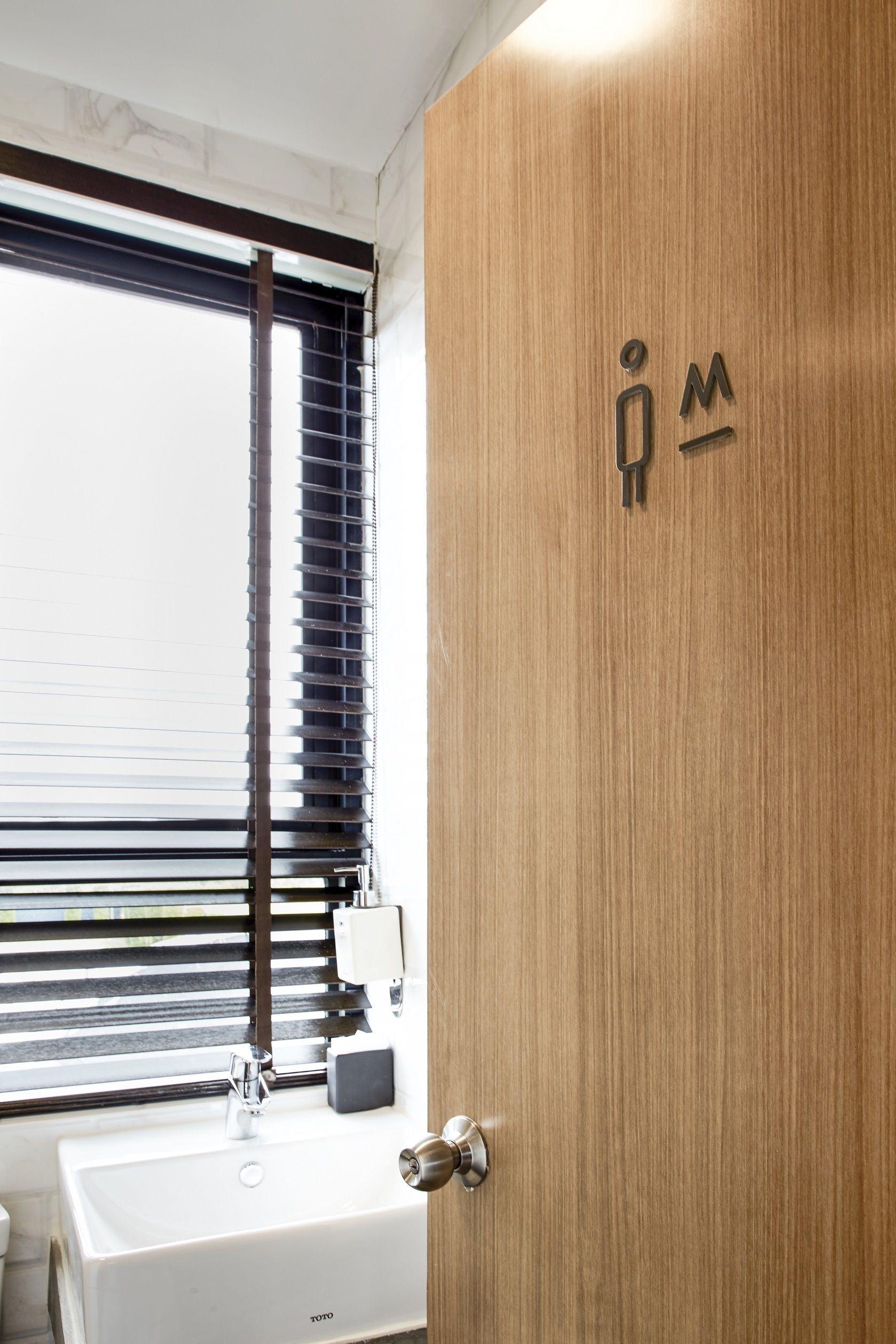 Un bagno moderno con una porta in legno, un lavabo bianco e una finestra con persiane.