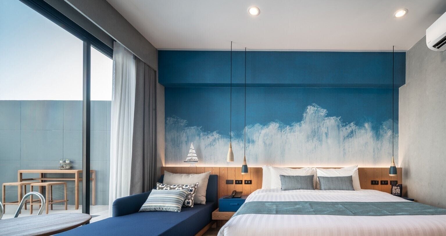 Une chambre d’hôtel moderne dotée d’un grand lit, d’un coin salon avec un canapé et des fauteuils, d’une petite table et d’une grande fenêtre.